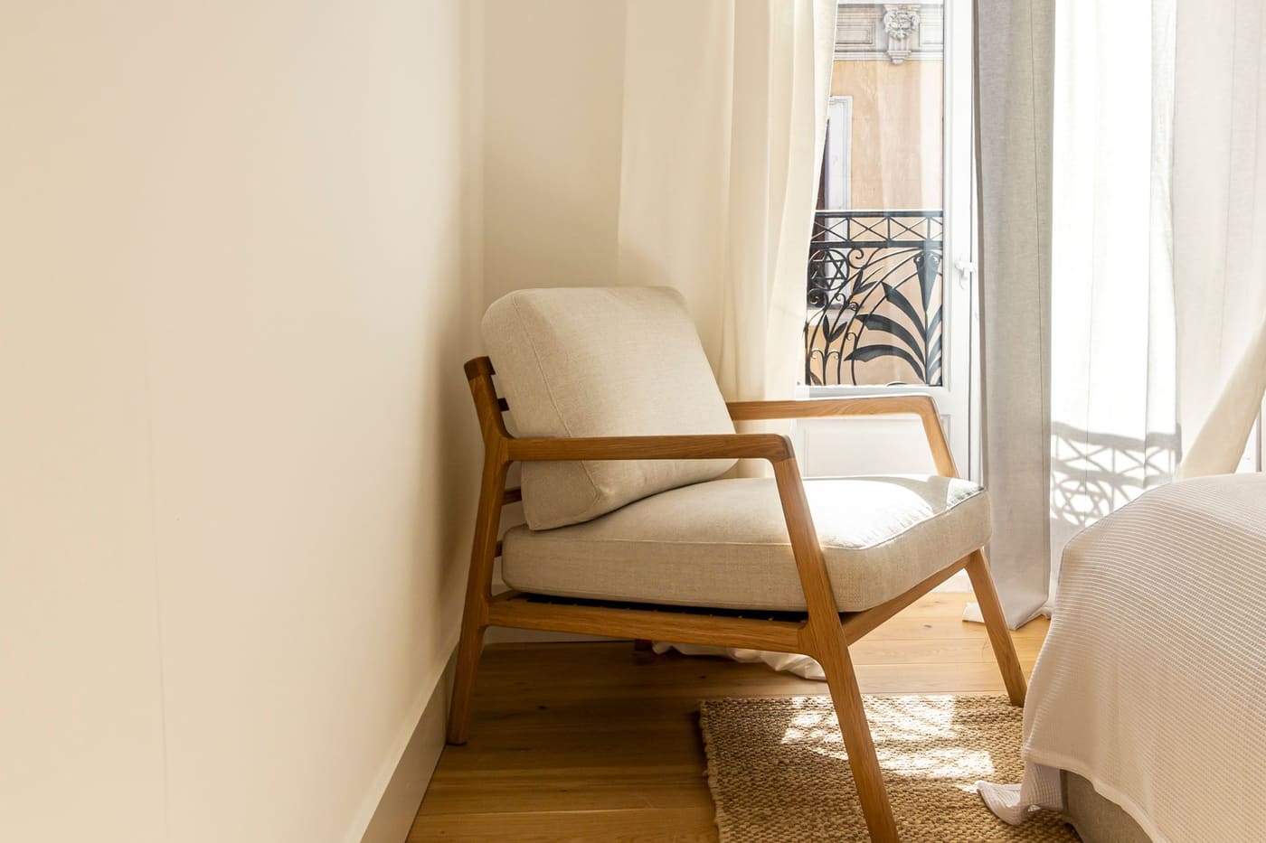 A cushioned wooden armchair in a bright corner beside a curtained window