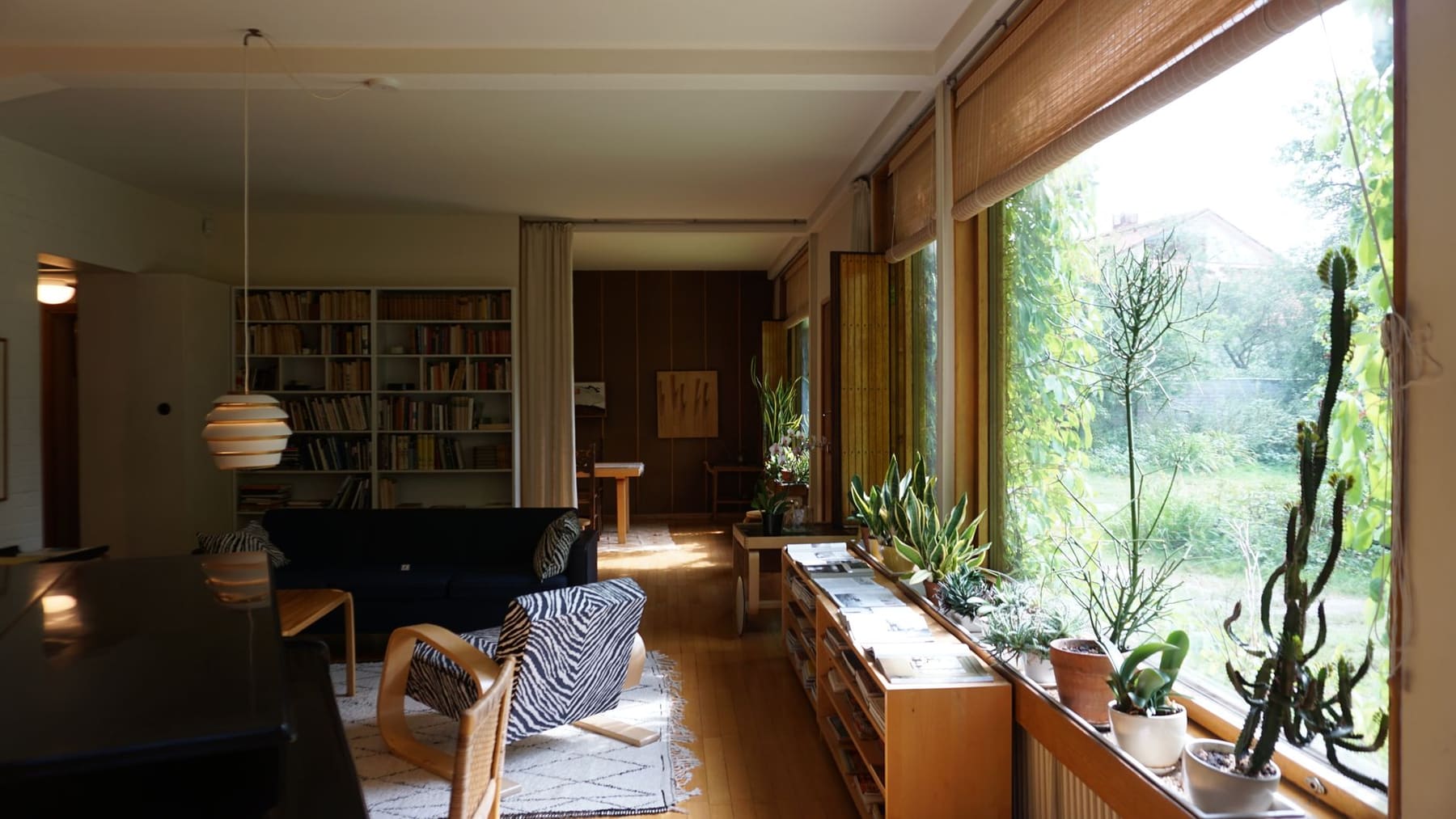 A bright, quiet living room with large windows, armchairs and houseplants