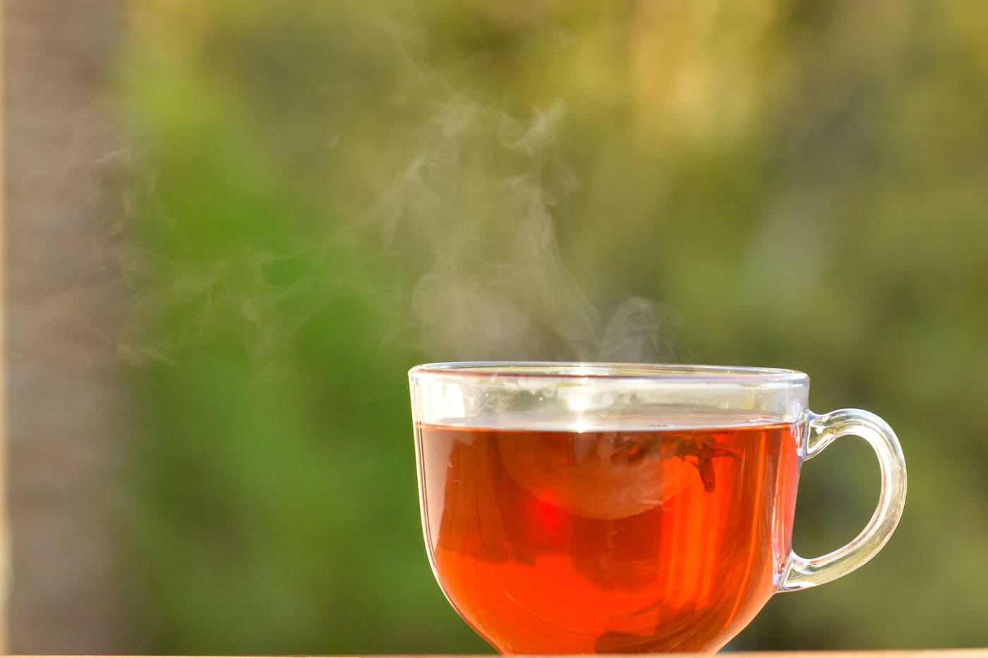 A clear glass mug of hot tea against a soft green blurred background
