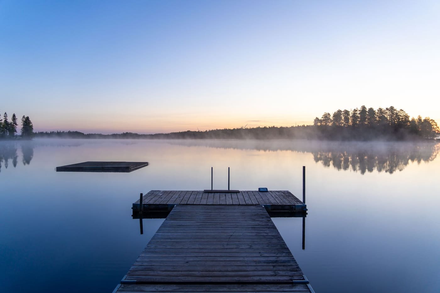 A wooden dock extending into a still lake at sunrise under a clear sky
