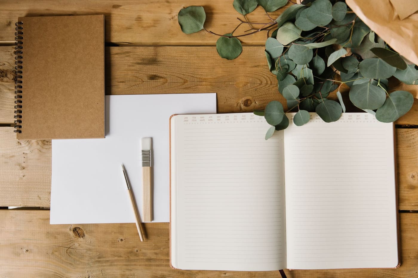 An open notebook and pencil on a wooden table with eucalyptus leaves