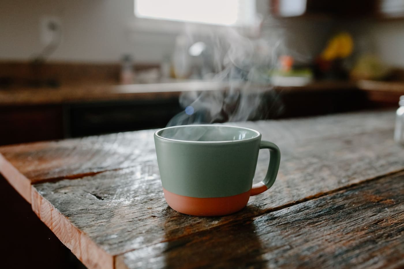 A steaming cup on a rustic wooden table in warm kitchen light