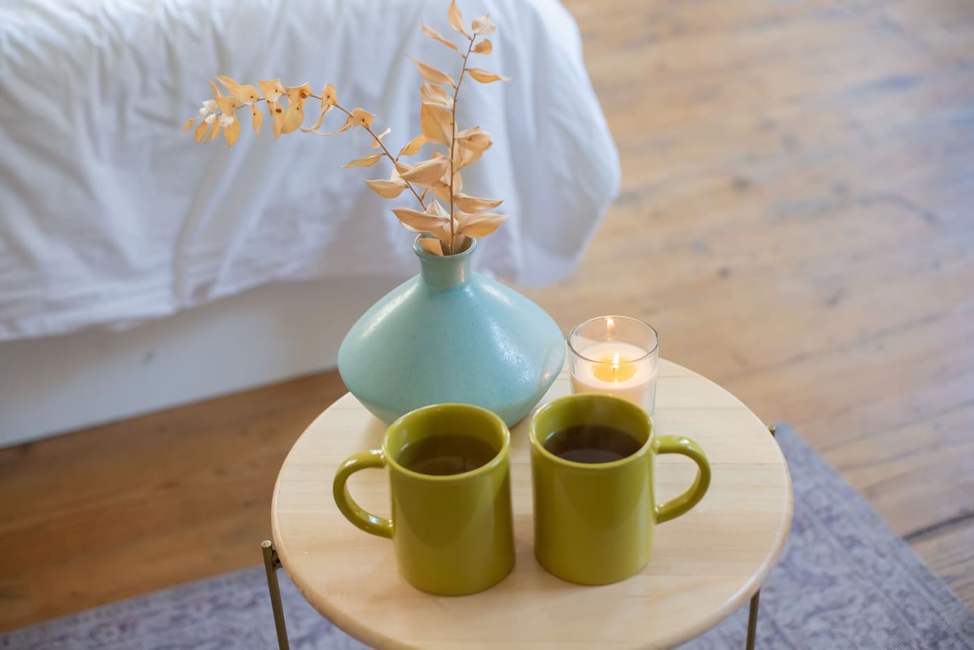 Two green mugs, a small vase and a candle on a round wooden side table